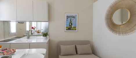 Un espacio habitable compacto con kitchenette, un sofá, una mesa de comedor con un plato y cubiertos, un espejo y un cartel en la pared.