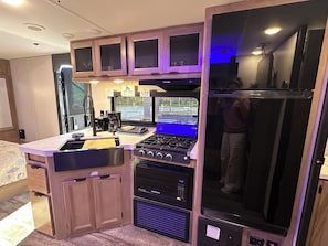 A compact kitchen with a gas stove, a microwave, and a refrigerator. - RV Oasis in Charming Downtown Deland (DeLand)