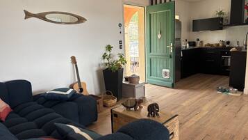 Een woonkamer met een bank, een gitaar, een spiegel in de vorm van een vis, een potplant en een houten kast.