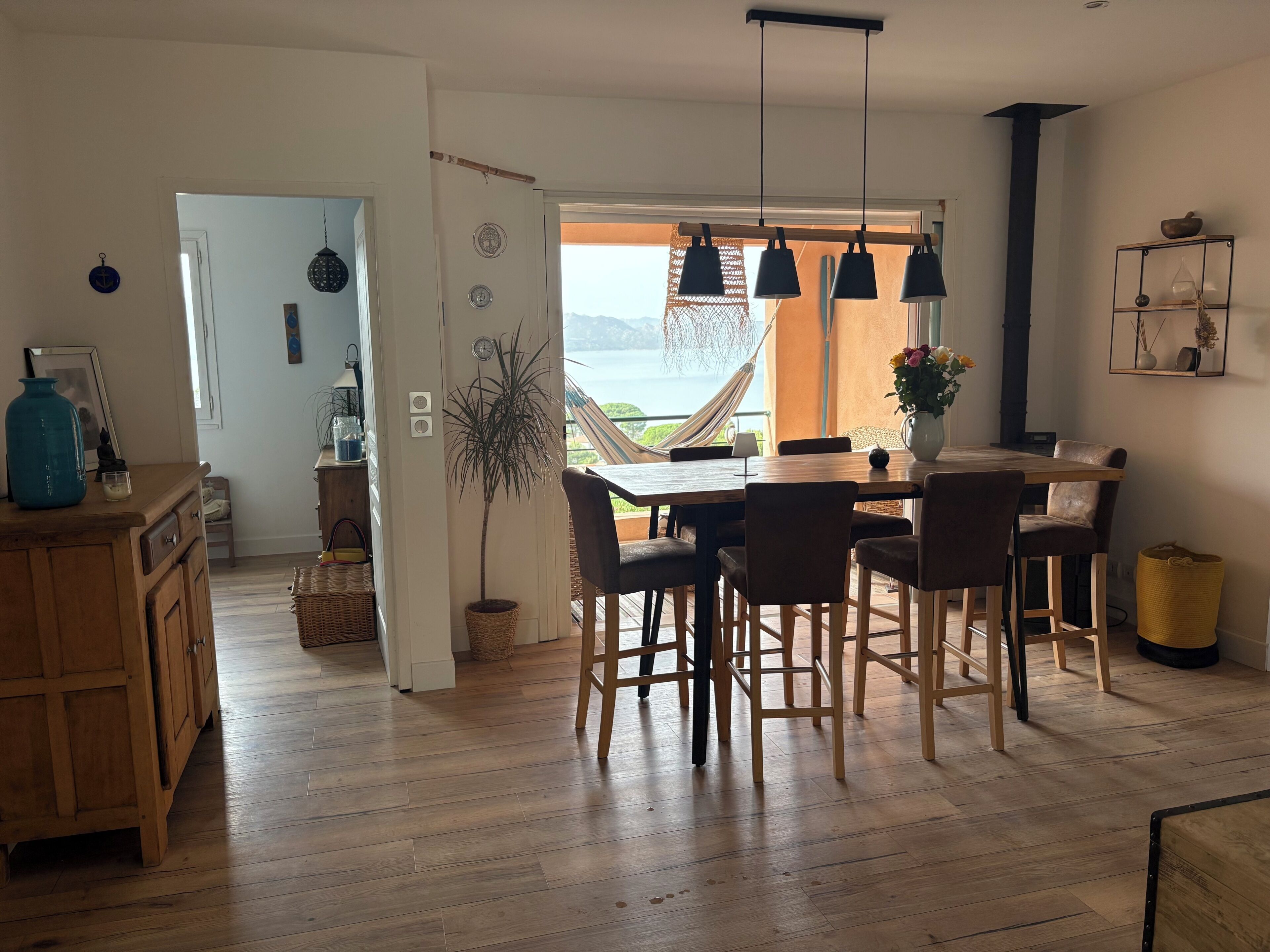 Een eethoek met uitzicht op zee, houten vloeren en een hangstoel bij het raam.