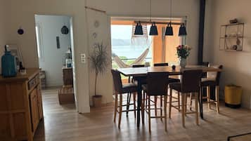 Een eethoek met uitzicht op zee, houten vloeren en een hangstoel bij het raam.