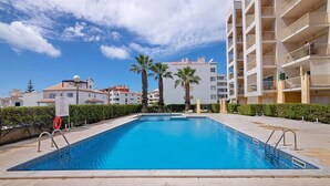 A swimming pool with a clear blue water, surrounded by a tiled deck and palm trees. - Apartment 'Algarve House' with Sea View, Wi-Fi and Air Conditioning (Albufeira)