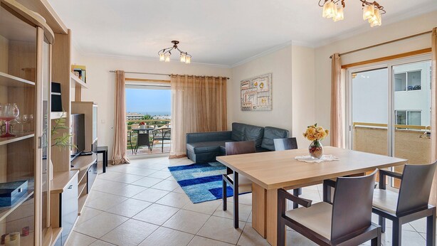 A modern living room with a sofa, dining table, and TV. There is a balcony with a view. - Apartment 'Algarve House' with Sea View, Wi-Fi and Air Conditioning (Albufeira)