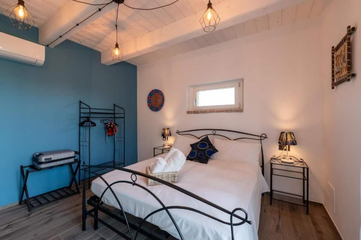 A bedroom with a bed, bedside tables, a window, and a wall-mounted air conditioner.