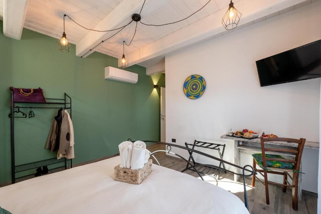 Habitación de hotel con cama, una pequeña mesa de comedor con sillas, televisor montado en la pared y perchero con ropa colgada.