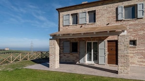 A two-story brick building with a covered patio, a wooden door, and a view of the sea. - Casa Addis B&B  (Senigallia)