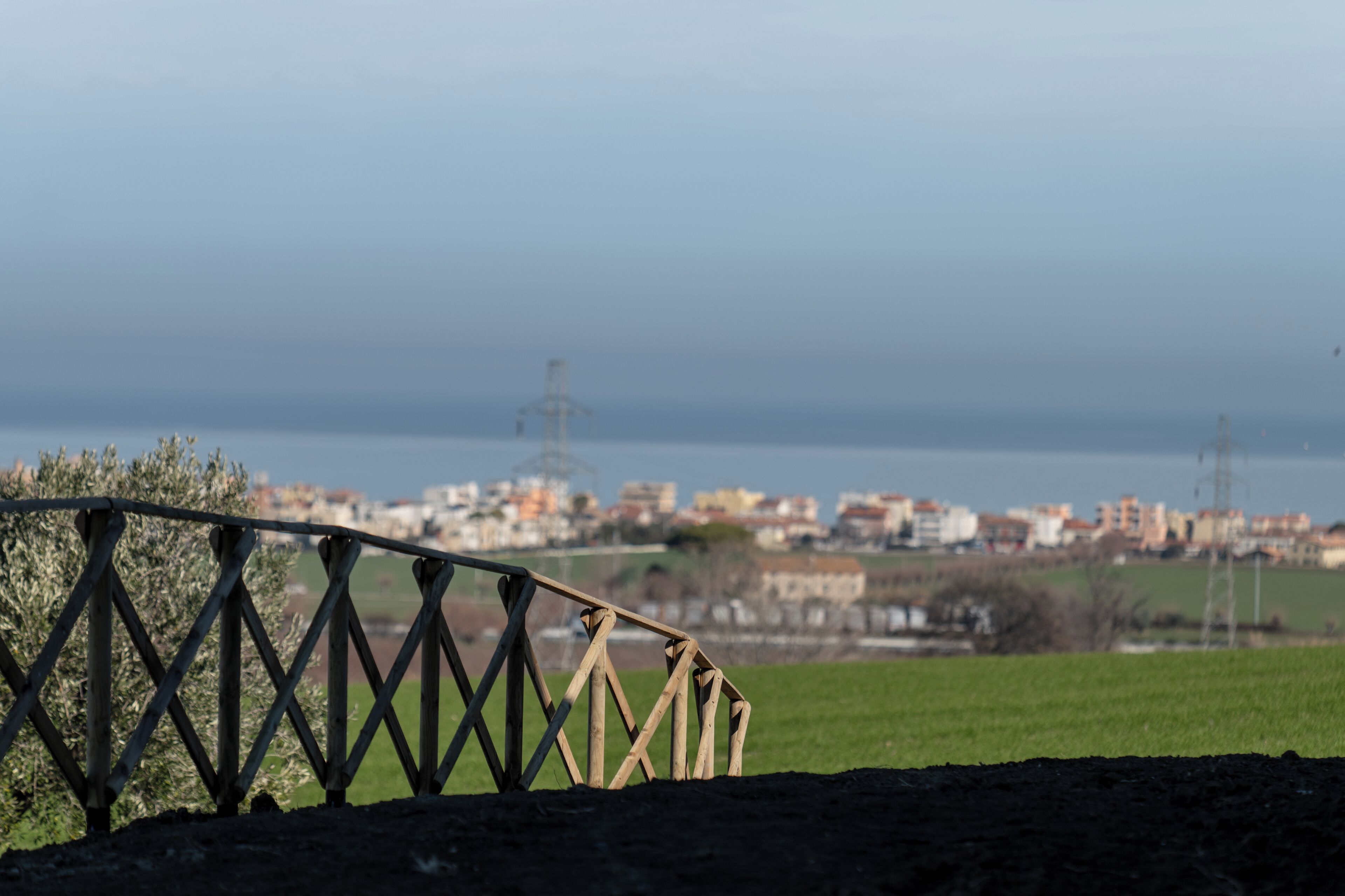 A coastal view with a wooden fence in the foreground, a clear sky, and a distant cityscape.