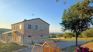 A stone building with a wooden play structure and a garden with flowers. - Casa Addis B&B  (Senigallia)