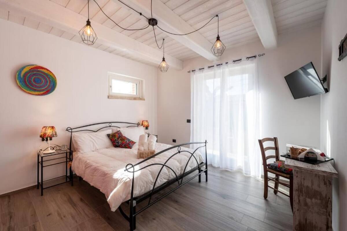 A bedroom with a bed, bedside lamps, a TV, a chair, and a desk.
