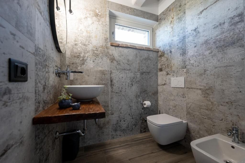 A bathroom with a stone wall, a wooden shelf with a basin, a toilet, and a bathtub.