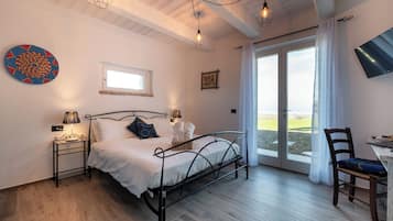 Un dormitorio con estructura de cama metálica, una mesita de noche con lámpara, una silla, un ventanal y vistas al exterior.