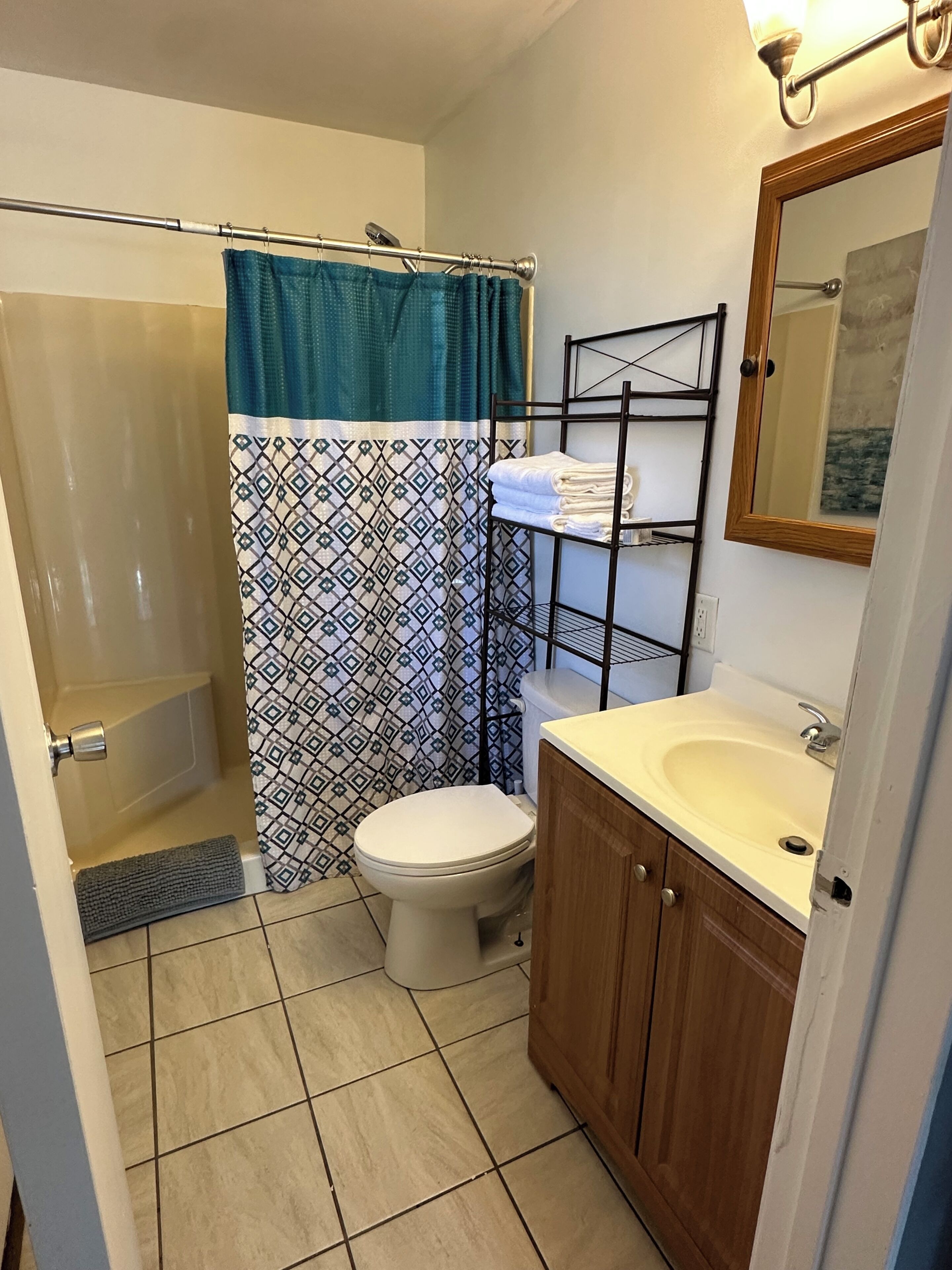 A bathroom with a shower, toilet, sink, and a towel rack.