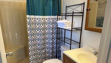 A bathroom with a shower, toilet, sink, and a towel rack.