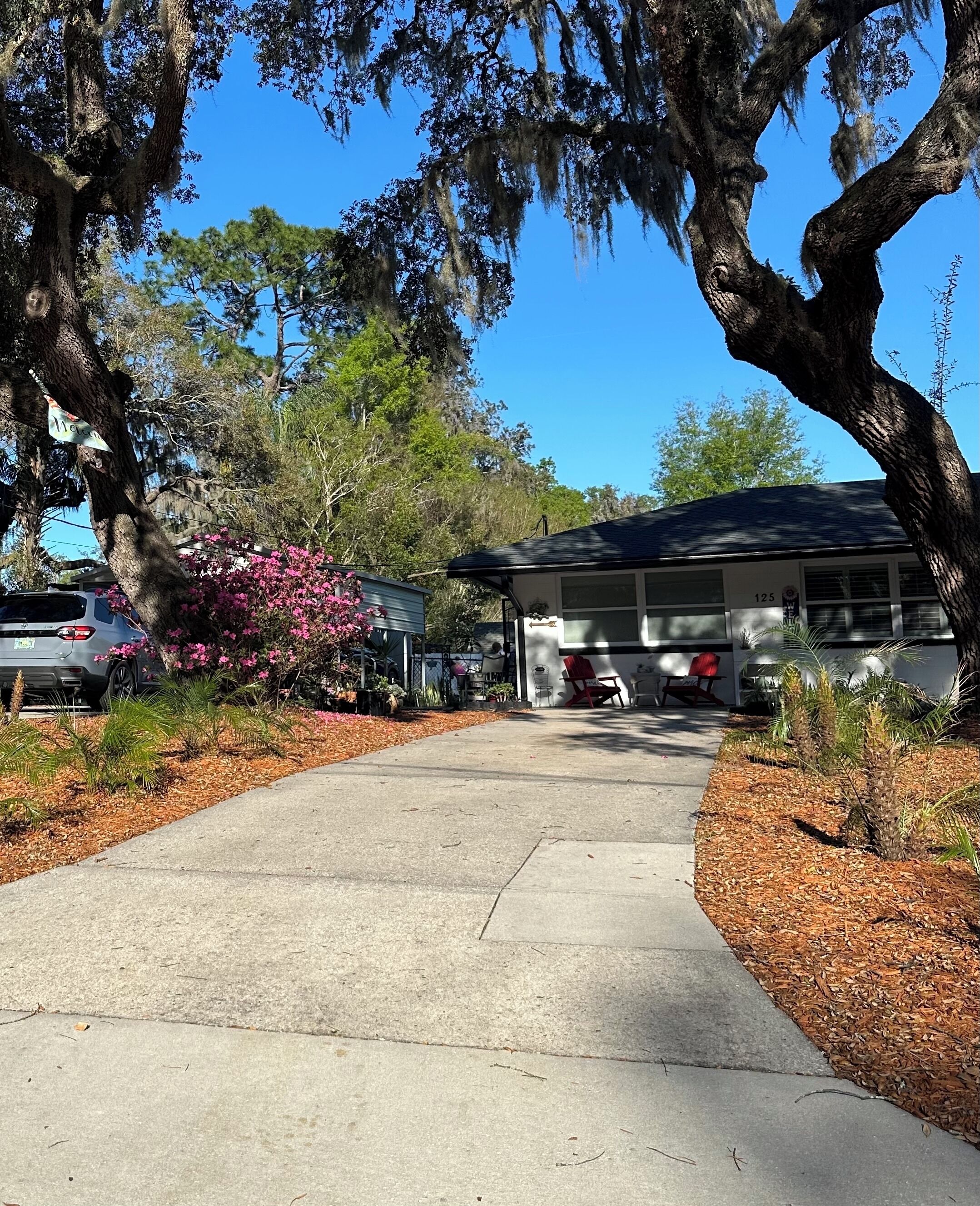 A driveway leading to a building with a number 125 sign, surrounded by trees and a parked car.