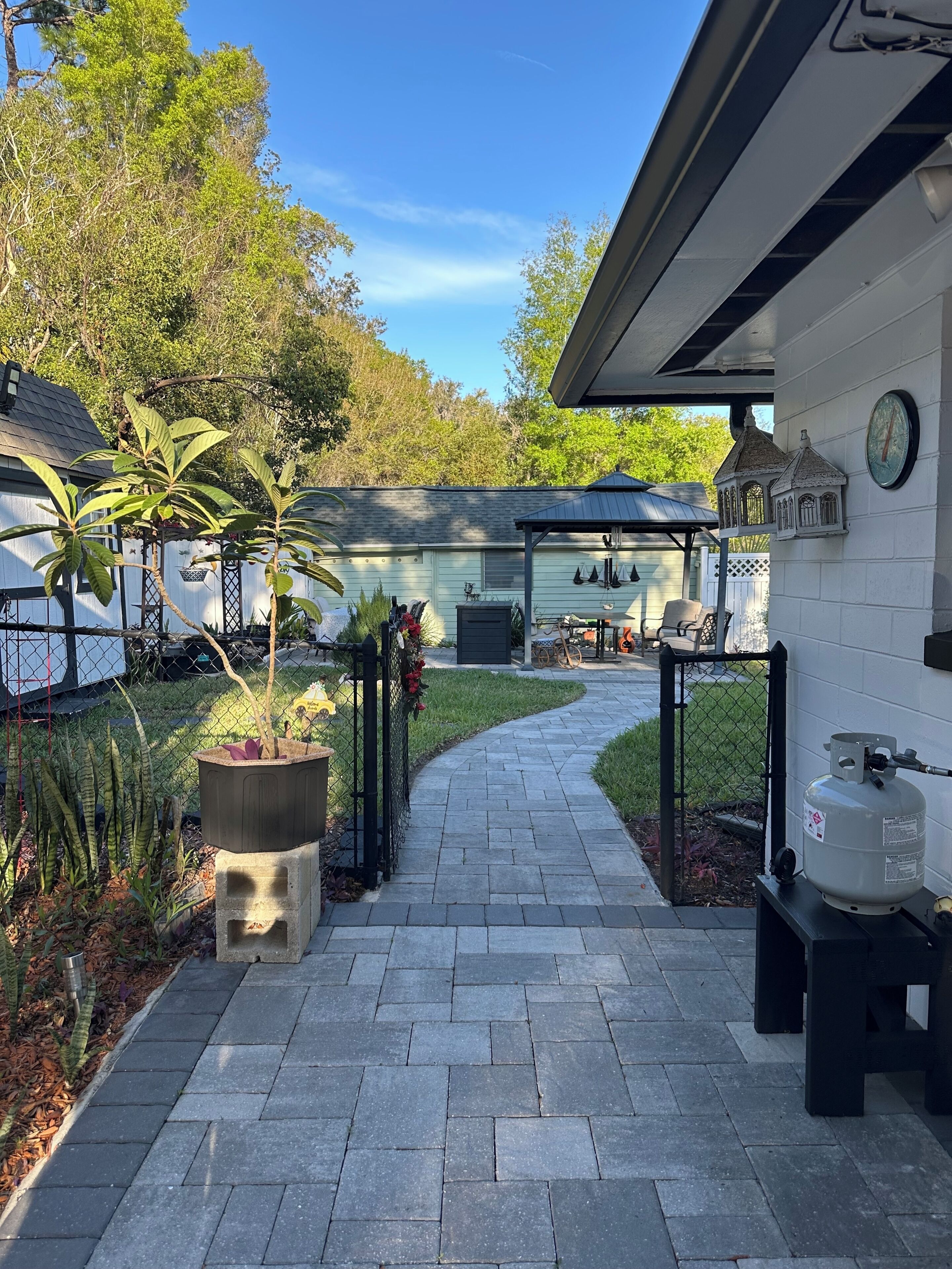 A paved pathway leading to a covered patio area with a grill and outdoor seating.