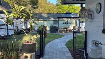 A paved pathway leading to a covered patio area with a grill and outdoor seating.