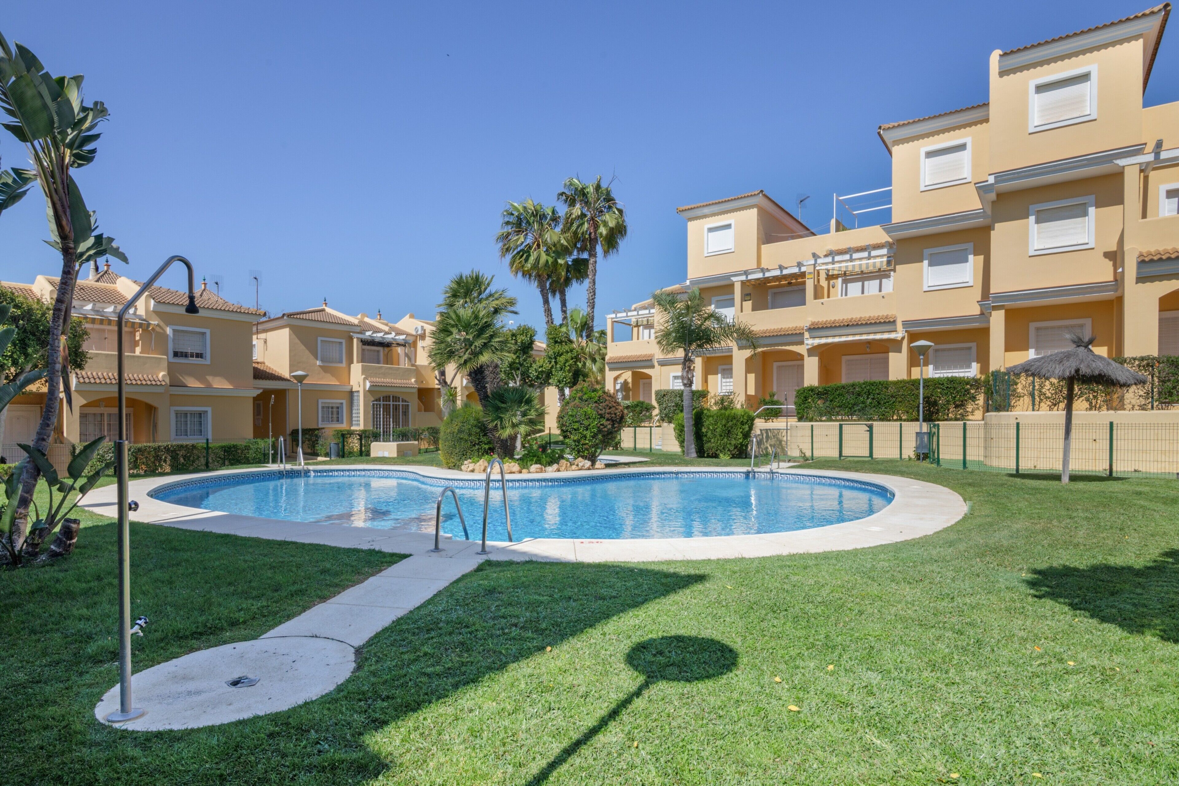 Una piscina rodeada de césped cuidado y palmeras, con un edificio con balcones al fondo.