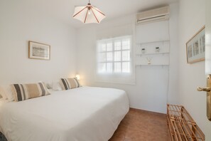 A bedroom with a bed, a window, a wall-mounted shelf with jars, and a hanging light fixture. - Penthouse in Islantilla with Shared Pool, Wi-Fi, and Air Conditioning (Huelva)