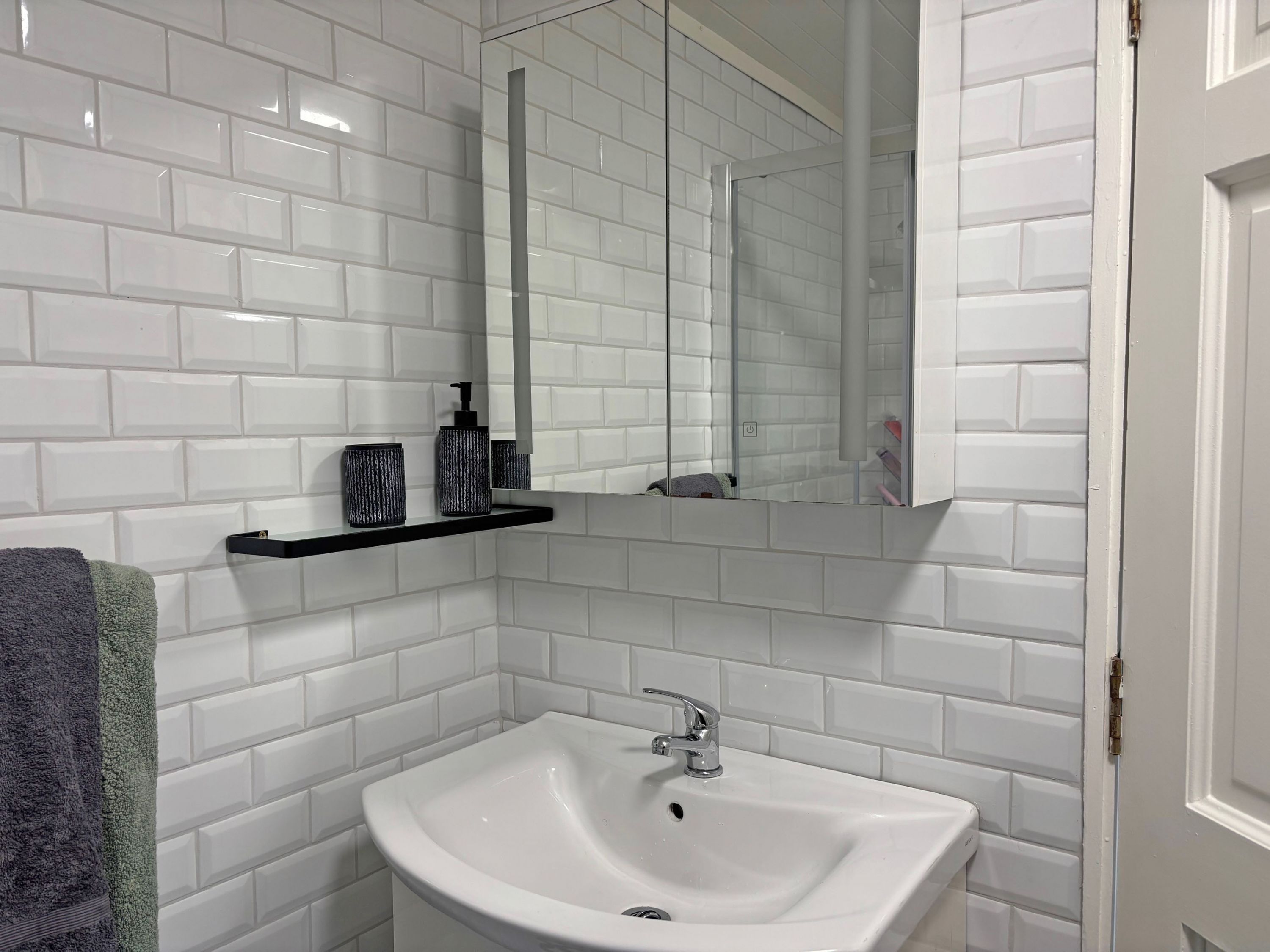 A bathroom with white subway tiles, a white sink with a chrome faucet, a mirror, and a towel rack with a towel.