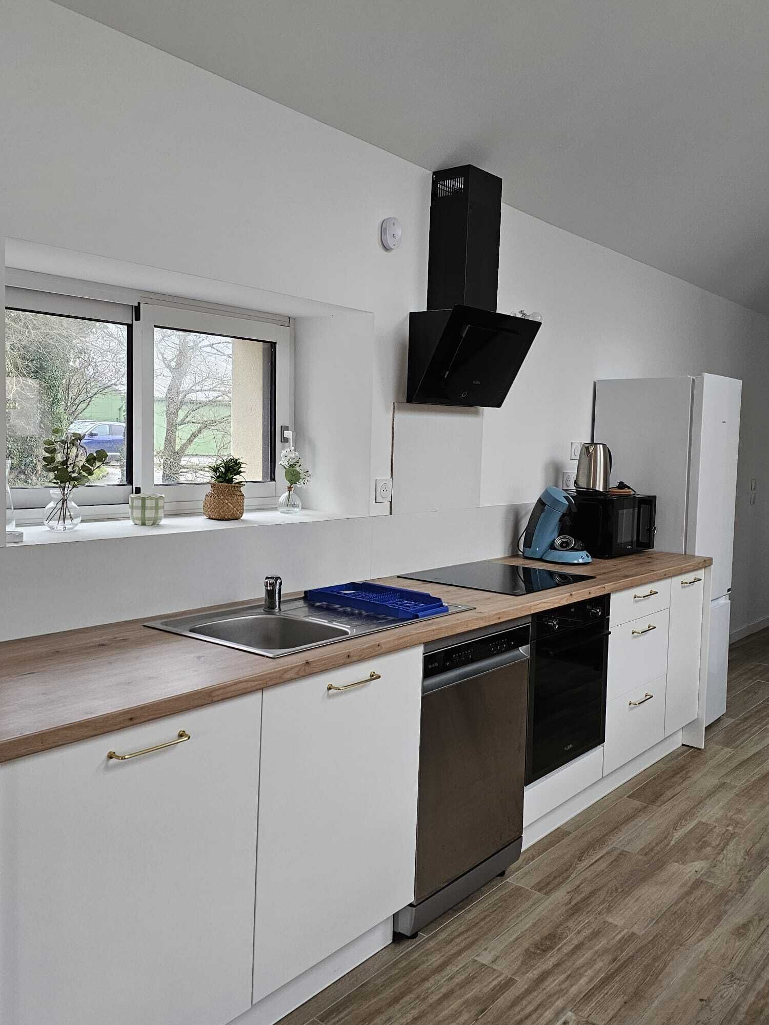 A modern kitchen with white cabinets, a black range hood, a window with a view, and a wooden countertop.