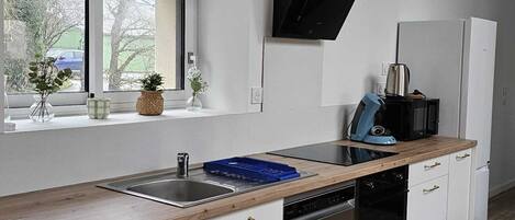 A modern kitchen with white cabinets, a black range hood, a window with a view, and a wooden countertop.