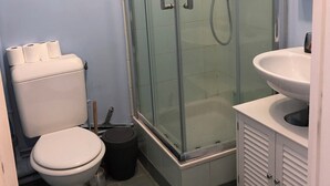 Un baño con inodoro, ducha con mampara de vidrio y lavamanos.