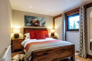 Een slaapkamer met een houten bed, rode kussens, een schilderij van een stier, twee bedlampjes en een raam met gordijnen.