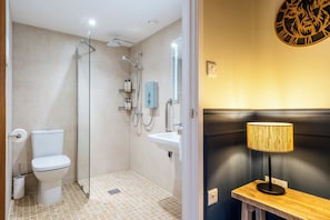 Een badkamer met een douche, toilet, wastafel en een houten bankje met een lamp.