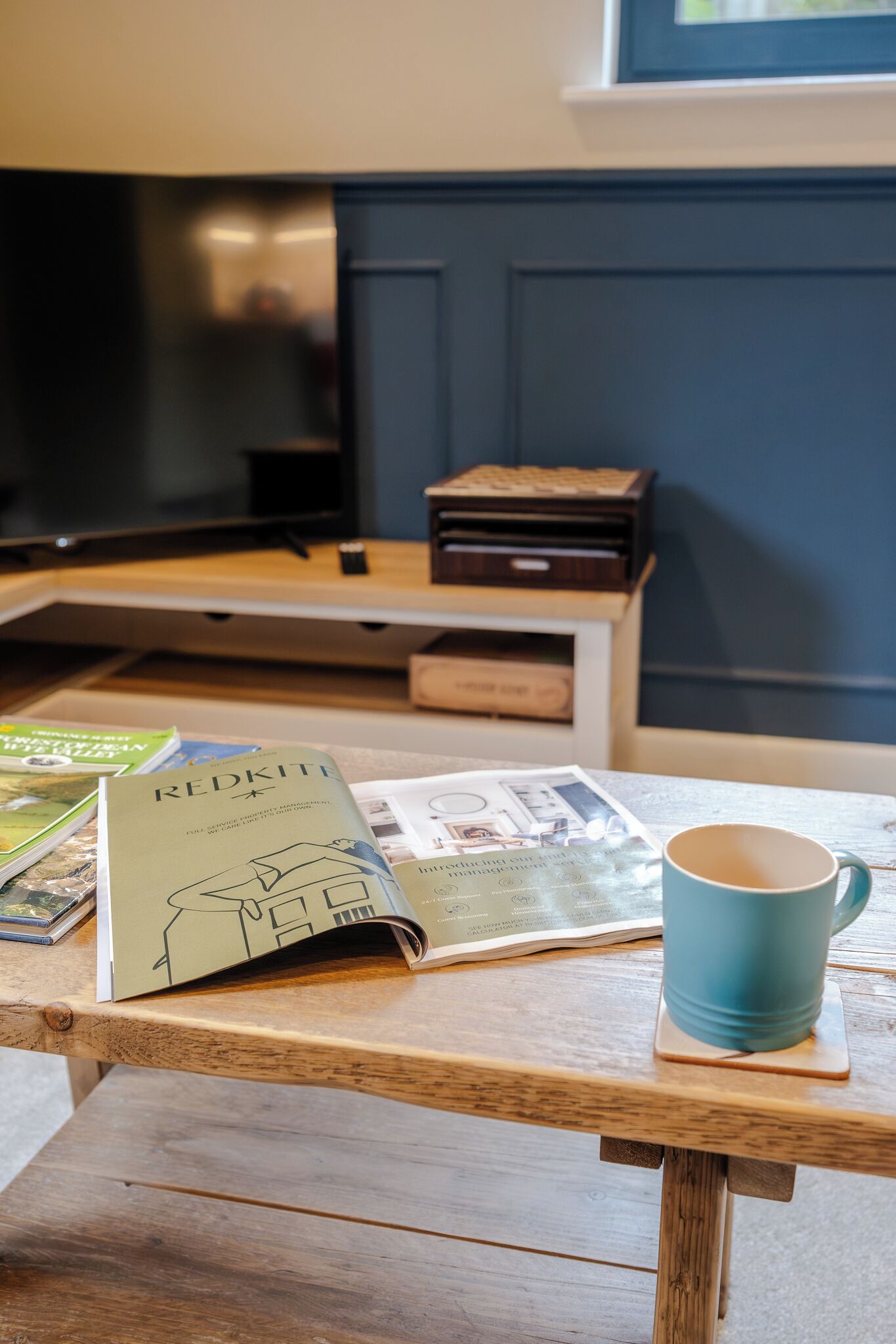 A wooden table with a blue mug, a book titled 'REDKITE,' and magazines.
