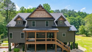 A large, two-story house with a covered porch and a staircase leading to a deck.