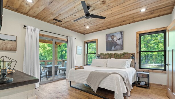 A bedroom with a bed, ceiling fan, wooden floor, and large windows.