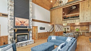 A spacious living area with a stone fireplace, a large blue sofa, and a kitchen in the background.