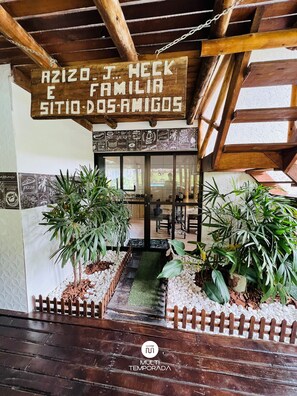 A restaurant entrance with a wooden sign, potted plants, and a tiled floor. - Sitío Rústico do Zizo com Piscina (Angelina)