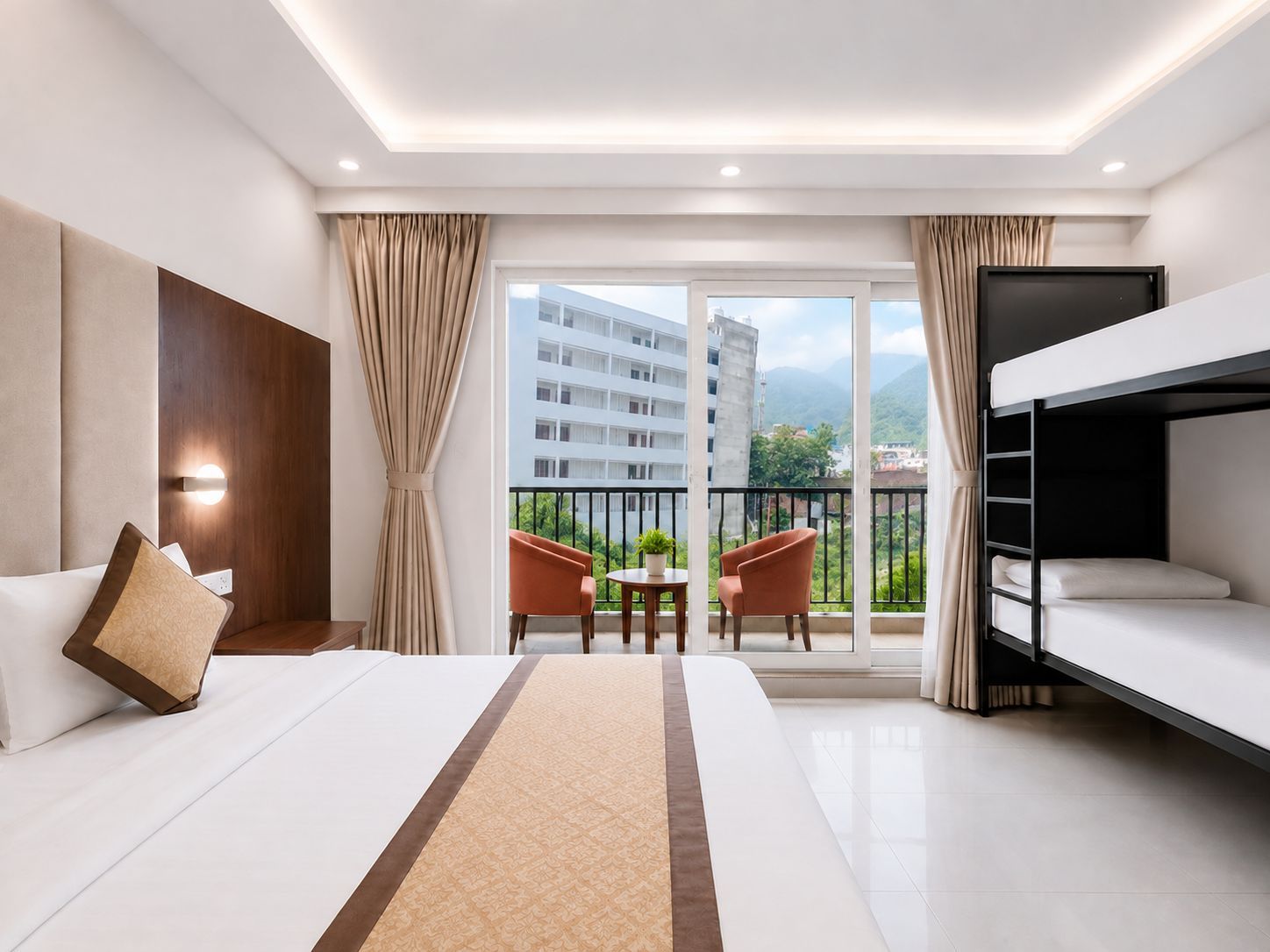 A hotel room with a bed, a sofa, a balcony with a table and chairs, and a view of a building and mountains.