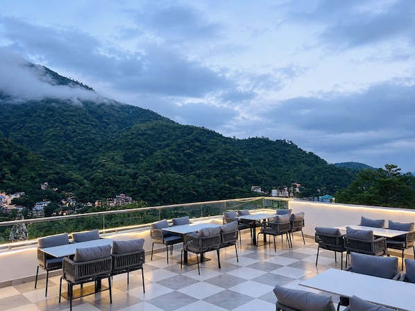 Una terraza al aire libre con mesas y sillas, con vistas a un paisaje montañoso.