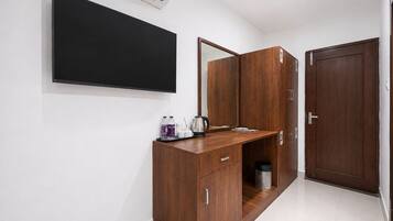 A hotel room with a flat-screen TV mounted on the wall, a wooden desk with a tray of toiletries, a mirror, and a wardrobe with a door marked '1'.