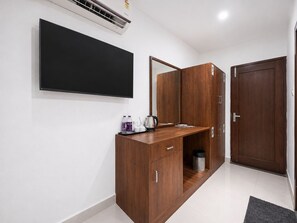 Habitación de hotel con televisor de pantalla plana en la pared, escritorio de madera con bandeja de artículos de aseo, espejo y armario con una puerta marcada '1'.