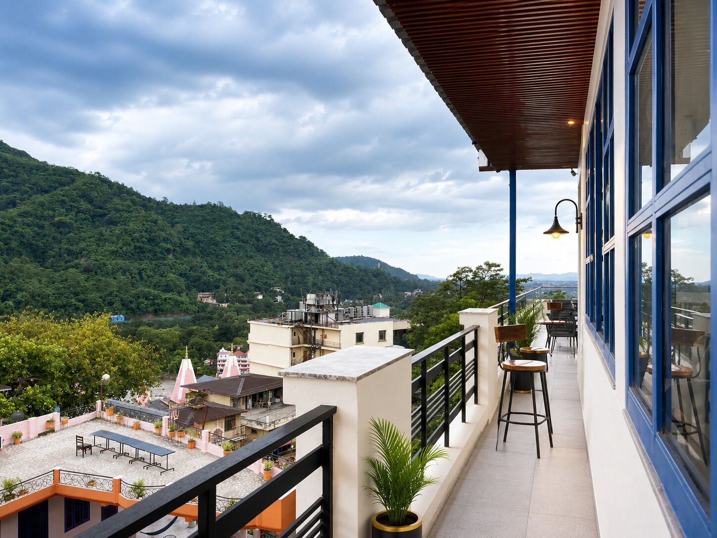 A balcony with a view of a mountainous landscape, a dining area with chairs and tables, and a railing.