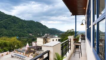 A balcony with a view of a mountainous landscape, a dining area with chairs and tables, and a railing.