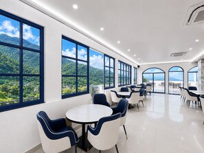 Un'ampia area interna con diversi tavoli e sedie, ampie finestre che offrono vista su un paesaggio montuoso e un design pulito e moderno.