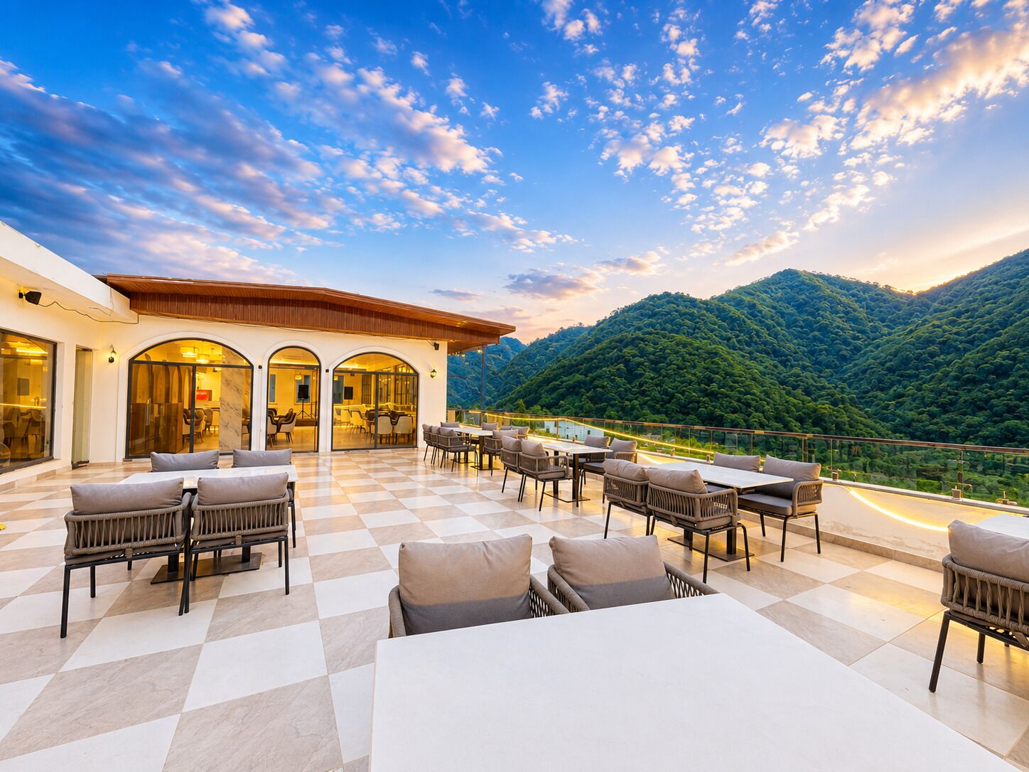 An outdoor terrace with checkered flooring, seating arrangements, and a view of a mountainous landscape.