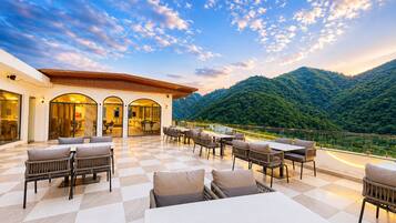 An outdoor terrace with checkered flooring, seating arrangements, and a view of a mountainous landscape.