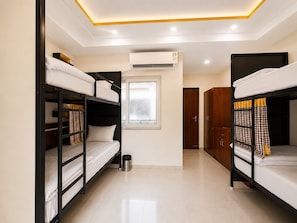 A dormitory room with bunk beds, a window, an air conditioning unit, and a door.