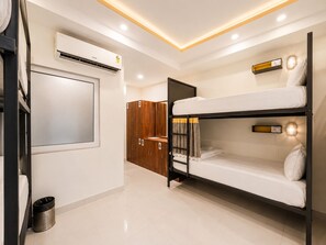 Habitación de hotel con literas, un armario, unidad de aire acondicionado, un cesto de basura y un espejo montado en la pared.