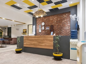 Zona de recepción con un mostrador de madera, pared de ladrillo, un reloj y dispensador de agua.