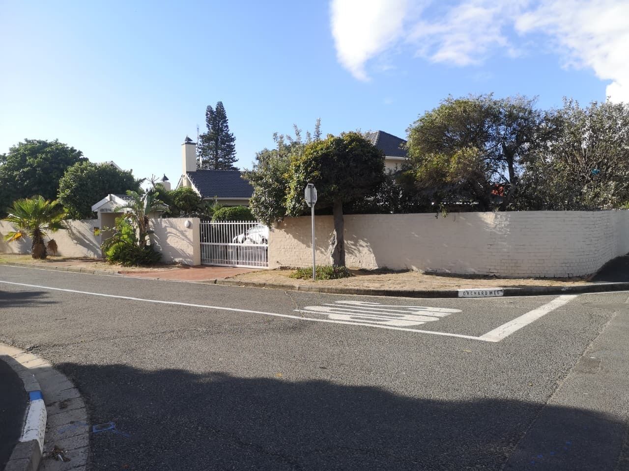 A street view with a pedestrian crossing, a white building with a grey roof, and a metal fence.