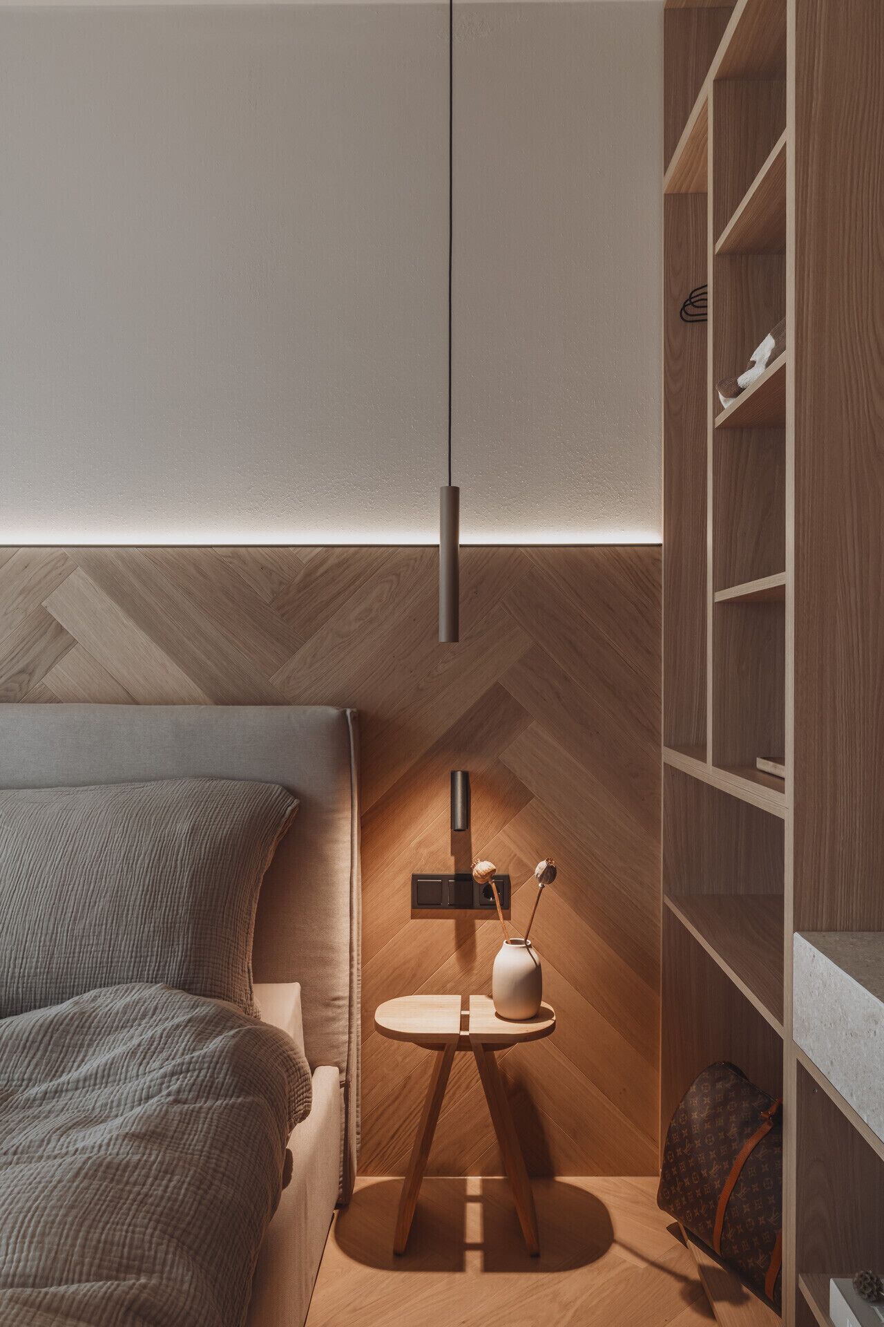 A modern bedroom with a bed, bedside table, lamp, and built-in wooden shelving.