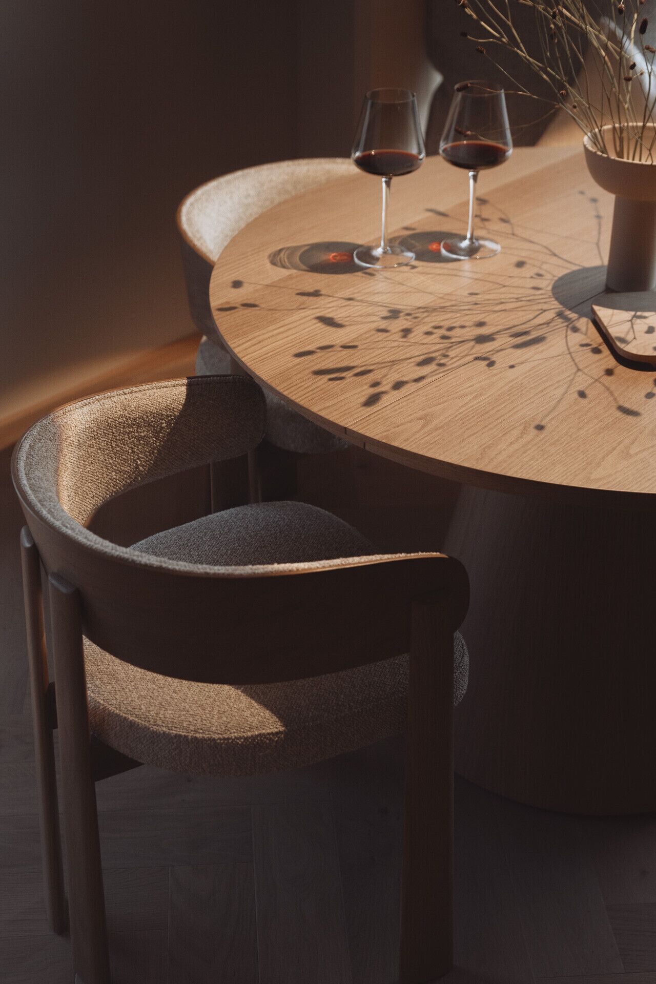 A round wooden table with two wine glasses and a vase with branches.