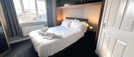A hotel room with a bed, a window with curtains, a radiator, and a wardrobe.