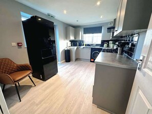 A modern kitchen with a built-in oven, a washing machine, and a dining area with a brown leather chair. - Elegant 4BDR Home with Private Parking in Darfield (Darfield)
